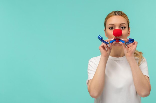 Aprilscherztag blondes Mädchenhaar Pferdeschwanz mit zwei Pfeifen rote Nase weißes T-Shirt Clown lustig