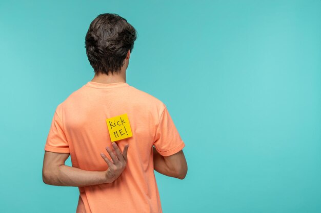 Aprilscherztag Typ von hinten, der versucht, den gelben Post-It-Aufkleber zu erreichen, trete mir das orangefarbene T-Shirt