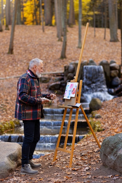 Kostenloses Foto aquarellmaler draußen im wald mit staffelei und leinwand