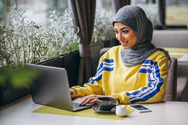 Arabische Frau im hijab innerhalb eines Cafés, das an Laptop arbeitet