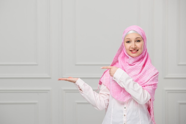 Arabisches Mädchen, hübsche, süße junge muslimische Frau, eingewickelt in einen schönen rosafarbenen Hijab, der nach links zeigt