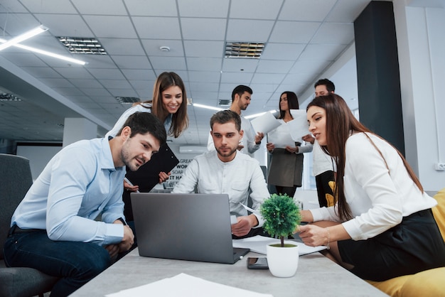 Arbeiten mit Laptop. Eine Gruppe junger Freiberufler im Büro unterhält sich und lächelt