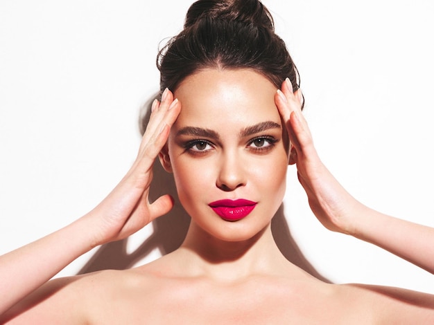 Arbeiten sie schönheitsporträt der jungen brunettefrau mit stilvollem abendmake-up und perfekter sauberer haut um sexy modell mit dem haar in einem brötchen, das im studio aufwirft mit den rosafarbenen hellen natürlichen lippen lokalisiert auf weiß