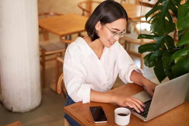 Arbeitende Unternehmerin, die im Café mit Laptop sitzt und auf dem Computer Kaffee trinkt