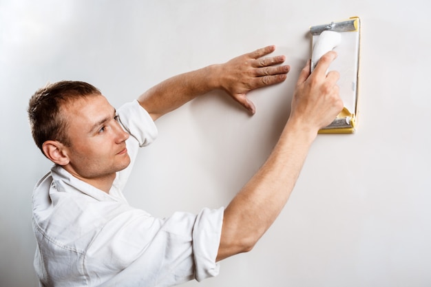 Arbeiter, der weiße Wand mit Sandpapier schleift.