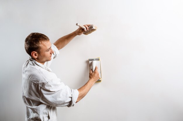 Arbeiter, der weiße Wand mit Sandpapier schleift.