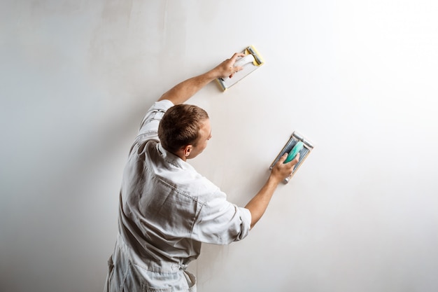 Kostenloses Foto arbeiter, der weiße wand mit sandpapier schleift.