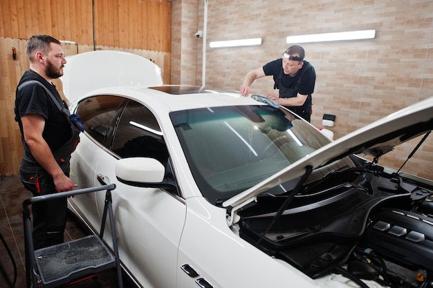 Arbeiter in der Detailing-Garage brachten Polyurethan-Antikies-Folienabdeckung in weißem Luxusauto an