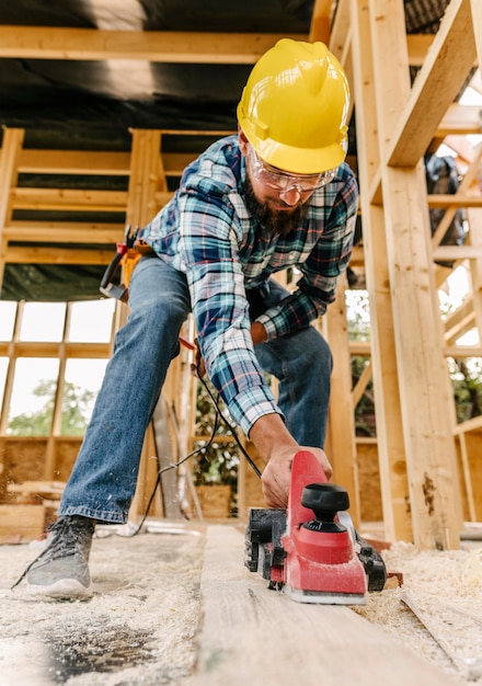 Arbeiter mit Schutzhelm, der Holzstück abschleift