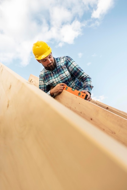 Arbeiter mit Schutzhelm und Wasserwaage überprüfen das Dachholz des Hauses