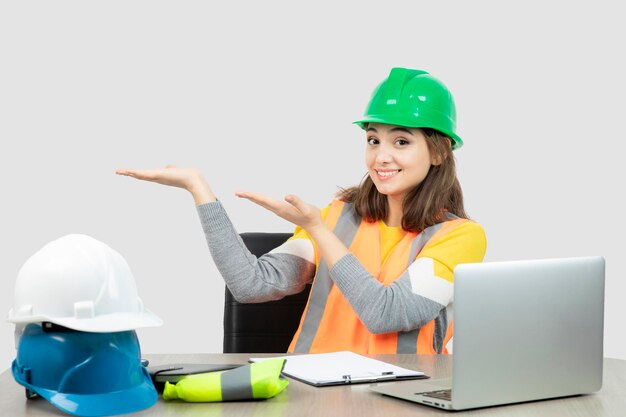 Arbeiterin in Uniform sitzt am Schreibtisch und zeigt geöffnete Handflächen. Foto in hoher Qualität