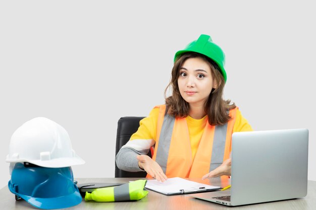 Arbeiterin in Uniform sitzt mit Laptop und Klemmbrett am Schreibtisch. Foto in hoher Qualität