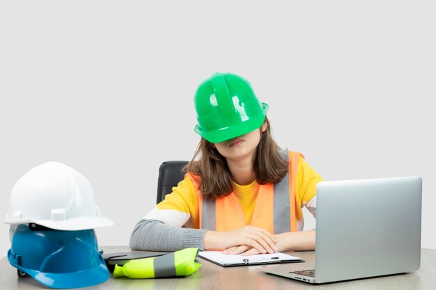 Arbeiterin in Uniform sitzt mit Laptop und Klemmbrett am Schreibtisch. Foto in hoher Qualität