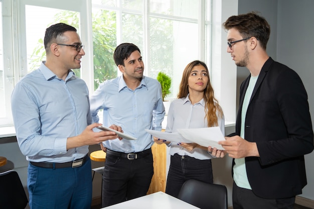 Arbeitsgruppe mit drei Mitarbeitern, die einem ernsthaften jungen Teamleiter Bericht erstatten