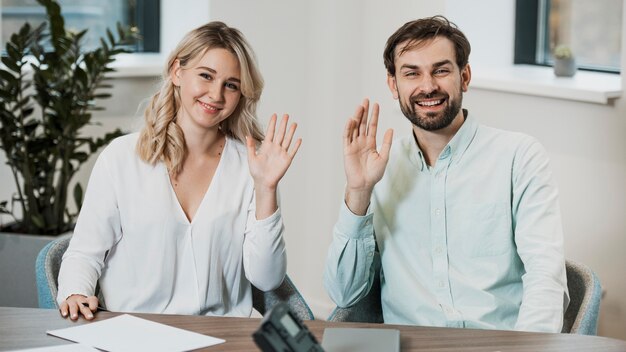 Arbeitskollegen winken und sitzen am Schreibtisch