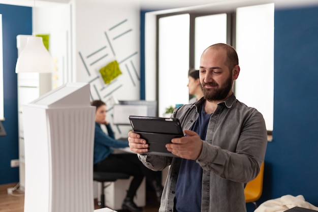 Arbeitsmanagermann, der auf tablet im architekturbüro schaut