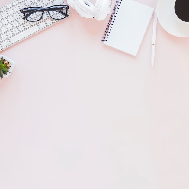 Arbeitsplatz mit verschiedenen Geräten, Notebook und Kaffeetasse auf rosa Hintergrund