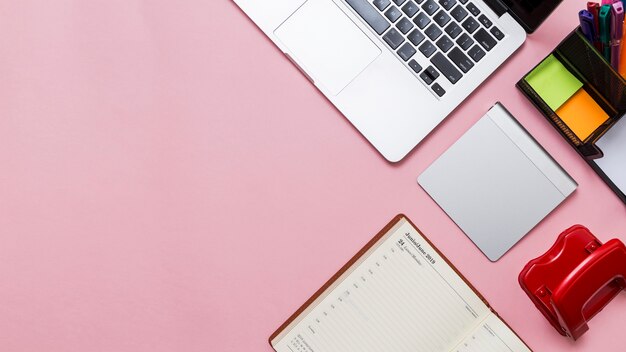 ArbeitsplatzBüroartikel und Laptop auf rosa Hintergrund