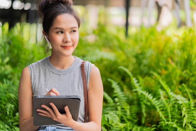 Arbeitstablett im öffentlichen Gartenpark Stadtstadt lifestlyeasian digitale Nomadenhand mit Tablet, die aus der Ferne arbeitet, mit positivem Gesichtsausdruck, lässig, intelligent, entspannt, Arbeit während der Reise im Garten