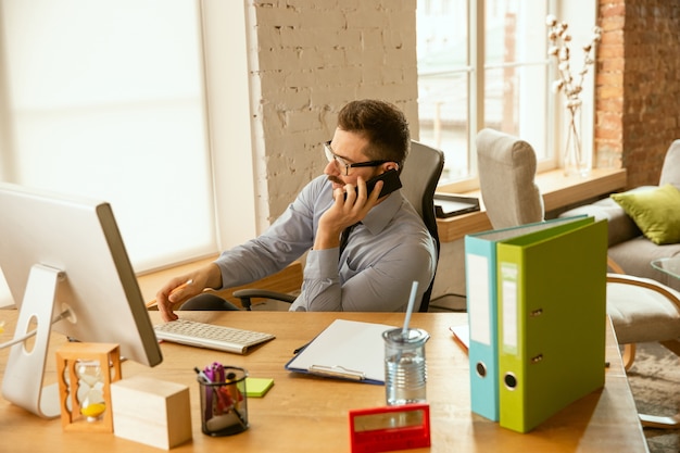 Arbeitszeit. Ein junger Geschäftsmann, der im Büro umzieht und einen neuen Arbeitsplatz bekommt. Junger männlicher Büroangestellter beim Verwalten nach der Beförderung. Sieht Glücklich aus