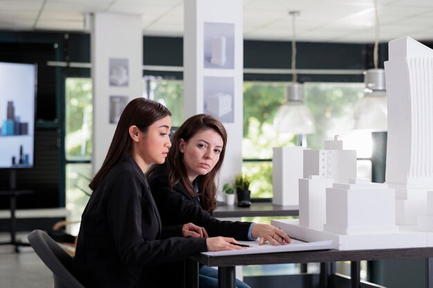 Architekten, die mit Blaupausen arbeiten, über das 3D-Druckmodell des Stadtbaus diskutieren, architektonisches Mock-up im Coworking Space. Mitarbeiter im Architekturbüro, Immobilienmakler, Ingenieure