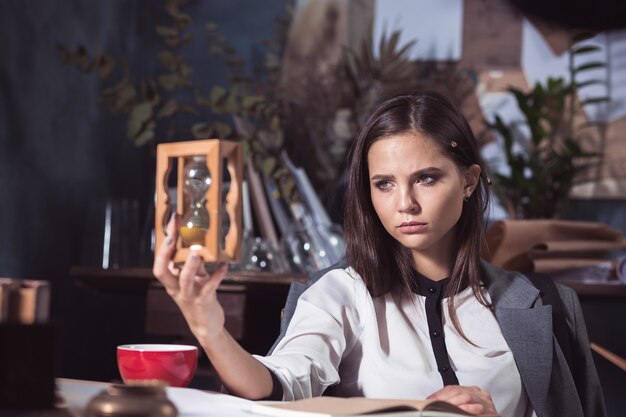 Architektin, die auf Zeichentisch im Büro oder zu Hause mit Sanduhr arbeitet. Konzept des Zeitmangels