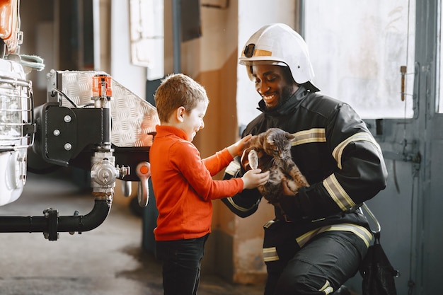 Arfican Feuerwehrmann in Uniform. Mann bereitet sich auf die Arbeit vor. Kerl mit Kind.