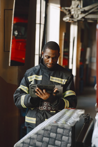 Arfican Feuerwehrmann in Uniform. Mann bereitet sich auf die Arbeit vor. Kerl mit Tablette.