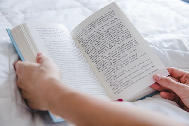 Arme mit Buch auf dem Bett