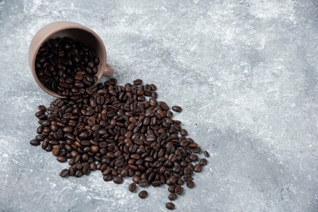 Aromatisch geröstete Kaffeebohnen aus der Tasse auf Marmoroberfläche.