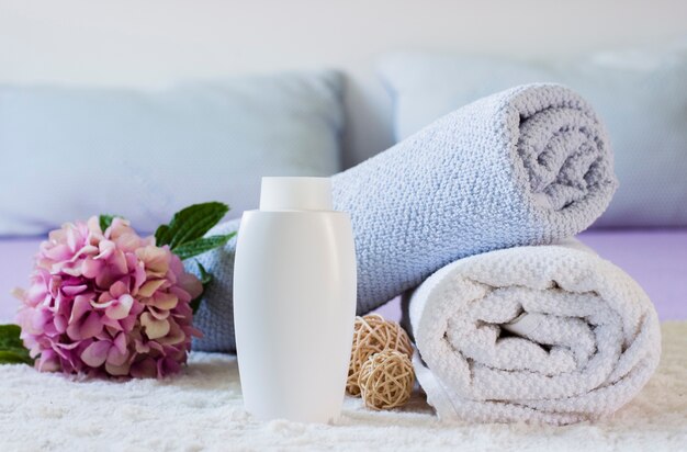 Arrangement mit Handtüchern, Flasche und Blume auf dem Bett