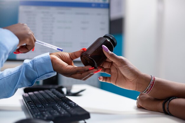 Arzt bietet Patienten während des Termines eine Medizinflasche über dem Klinikschreibtisch an. Klinische Konsultation einer Frau durch einen Arzt, der Medikamente im Krankenhauskabinett verschreibt.