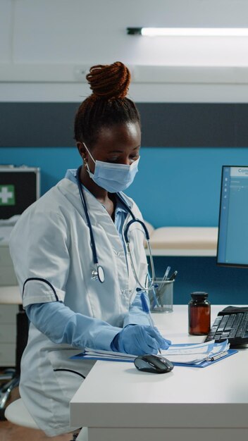 Arzt, der dem Patienten bei der ärztlichen Untersuchung verschreibungspflichtige Medikamente gegen Krankheit gibt. Frau, die Papier und eine Flasche Pillen für die medizinische Behandlung erhält und während einer Pandemie eine Gesichtsmaske trägt