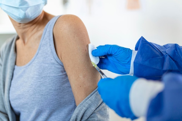 Arzt, der eine Spritze hält, die eine covid 19-Impfungs-Injektionsdosis in der Schulter einer Patientin mit Maske macht Grippe-Influenza-Impfstoff klinische Studien Konzept Corona-Virus-Behandlung Nahaufnahme