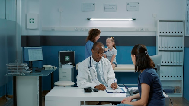 Arzt, der sich mit einem Erwachsenen im medizinischen Kabinett unterhält und sich Notizen zur Gesundheitsdiagnose macht. Hausarzt im Gespräch mit Mutter über Genesungsbehandlung bei Termin.