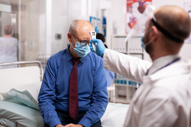 Arzt hält ein digitales Thermometer an die Stirn des Patienten und überprüft die Temperatur während der Coronavirus-Pandemie