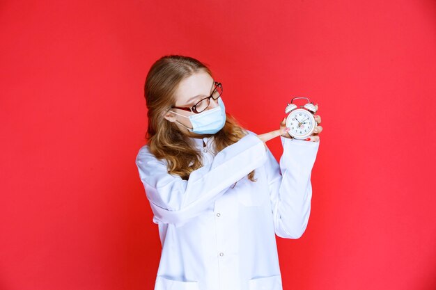 Arzt in Gesichtsmaske, der eine Uhr zeigt, die die Zeit für die Einnahme von Medikamenten bedeutet.