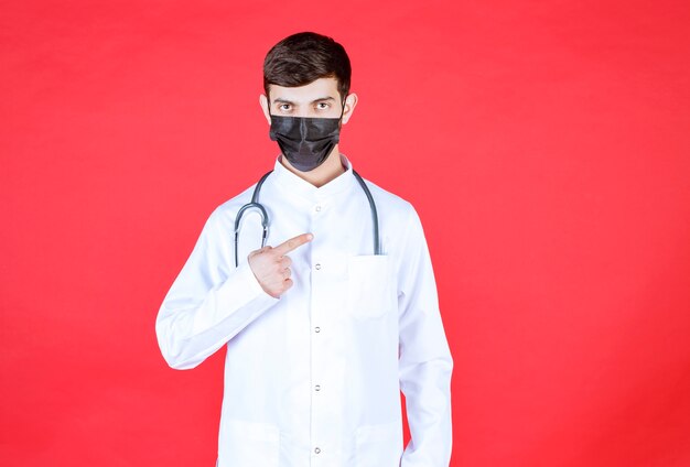 Arzt in schwarzer Maske mit Stethoskop am Hals.