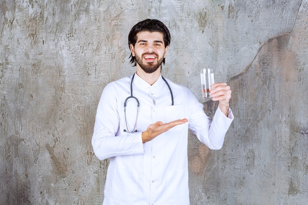 Arzt mit einem Stethoskop, der ein Glas reines Wasser hält und irgendwo hinzeigt