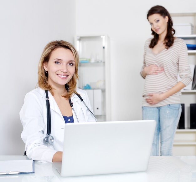 Arzt mit Laptop und junger schwangerer Frau im Krankenhaus - drinnen