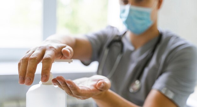 Arzt mit medizinischer Maske mit Händedesinfektionsmittel