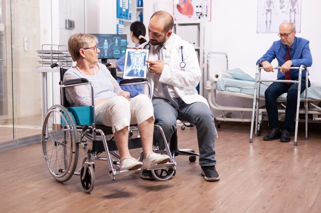 Arzt mit Stethoskop mit Tablet-PC während der Untersuchung einer behinderten Frau im Rollstuhl