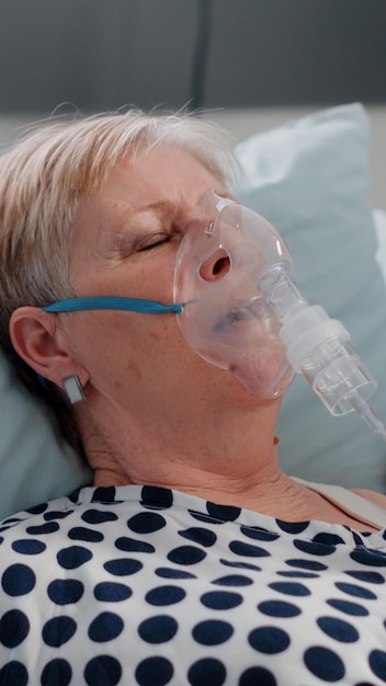 Arzt und Krankenschwester helfen schwer atmenden Frauen mit Sauerstoffschlauch, um Atemprobleme im Bett zu heilen. Medizinisches Team hilft älteren Patienten mit hyperventilierender Krankheit.