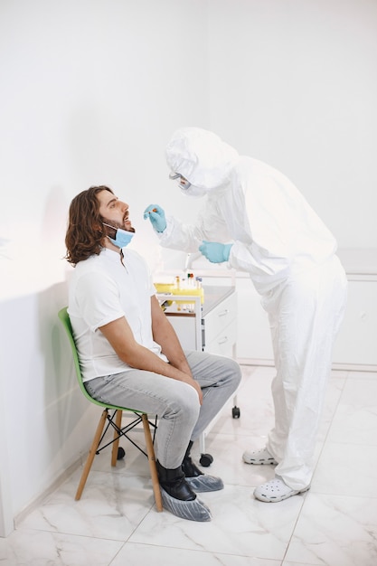 Arztschutzanzug und chirurgische Gesichtsmaske. Wattestäbchen aus Hals und Nase des Patienten. Coronavirus-Test, Test auf Covid-19-Infektion bei einer Pandemie.