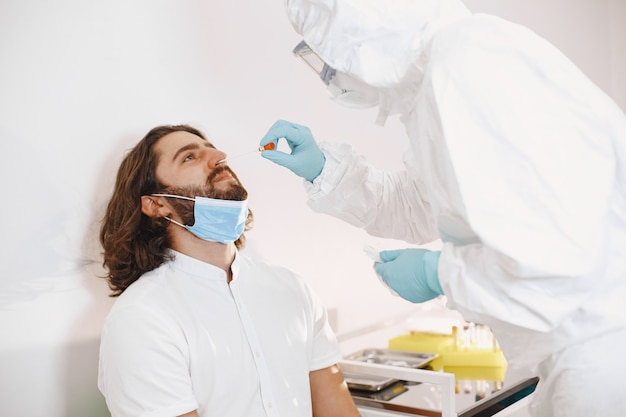 Arztschutzanzug und chirurgische Gesichtsmaske. Wattestäbchen aus Hals und Nase des Patienten. Coronavirus-Test, Test auf Covid-19-Infektion bei einer Pandemie.