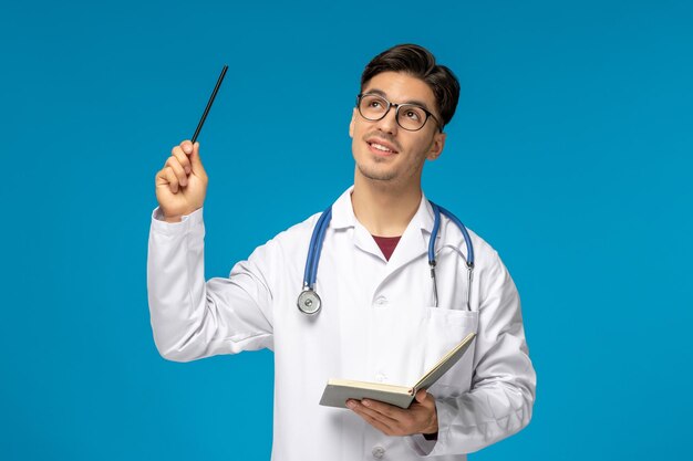 Arzttag süßer junger gutaussehender mann im laborkittel und brille mit stift und notizbuch
