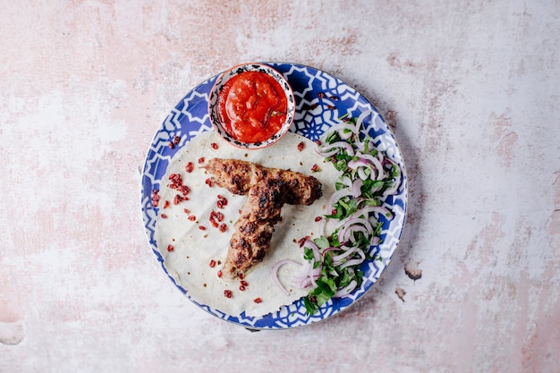 Aserbaidschanischer Lebensmittel Lule Kebab mit Kräutern und Bbq-Soße innerhalb der dekorativen Platte.