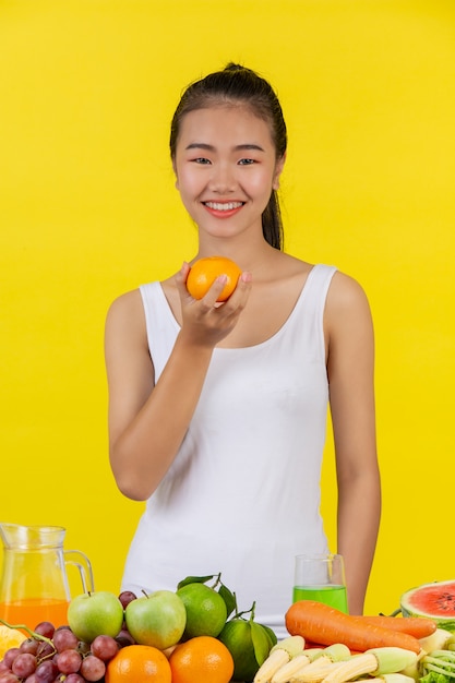 Asiatin Halten Sie Orangen mit der rechten Hand, und auf dem Tisch liegen viele Früchte.