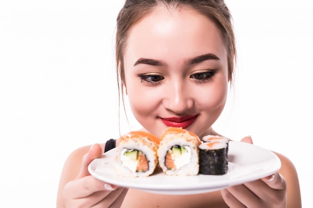 Asiatin mit bescheidener Frisur sitzt auf dem Tisch und isst lächelnd Sushi-Rollen