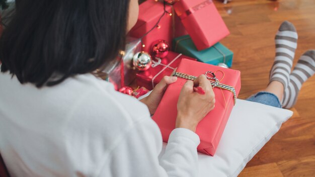 Asiatinnen feiern Weihnachtsfest. Weibliche jugendlich Abnutzungsstrickjacke und Sankt-Hut entspannen sich glückliches schreiben einen Wunsch auf Geschenk nahe Weihnachtsbaum genießen Weihnachtswinterurlaube zusammen in Wohnzimmer zu Hause.